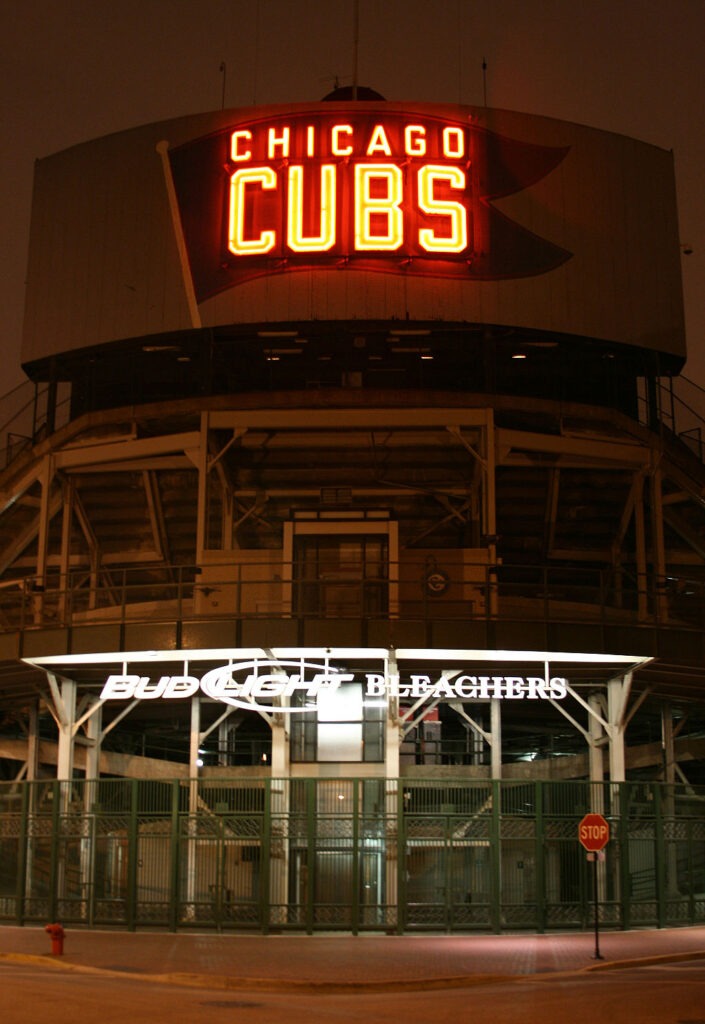 Bleachers Entrance to Wrigley Field at Night, with the words "Chicago Cubs" lit up in red, fluorescent letters.