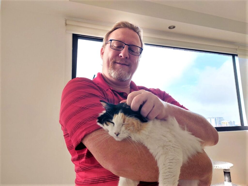 David holding one of our house sit cats while scratching its head in Guatemala. The cat's eyes are closed in contentment.