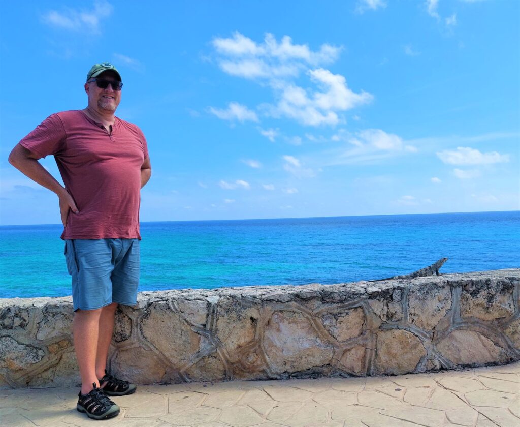 David on a Malecon on Isla Mujeres with an iguana next to him
