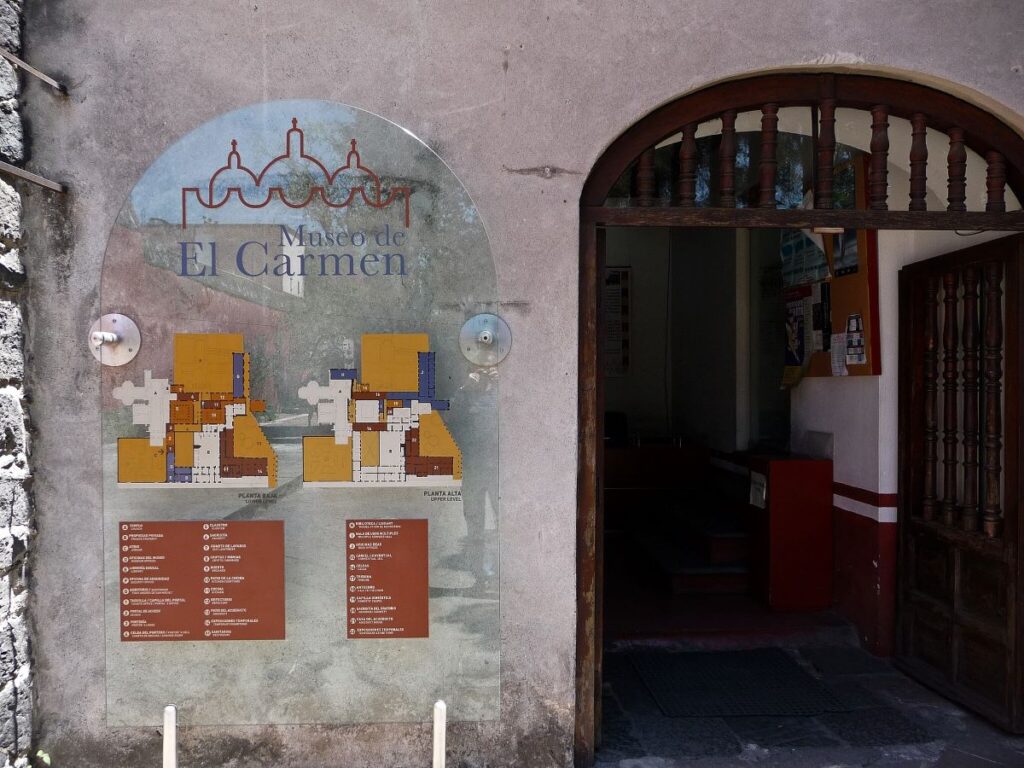 Entrance to Museo El Carmen in Mexico City, with a map of the premesis to the left of the arched, wooden doorway.