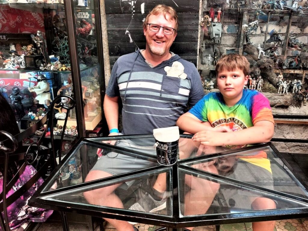 David and Little Man sitting at a tie fighter shaped table surrounded by Star Wars themed memorabilia at a Star Wars themed restaurant in Mexico City.