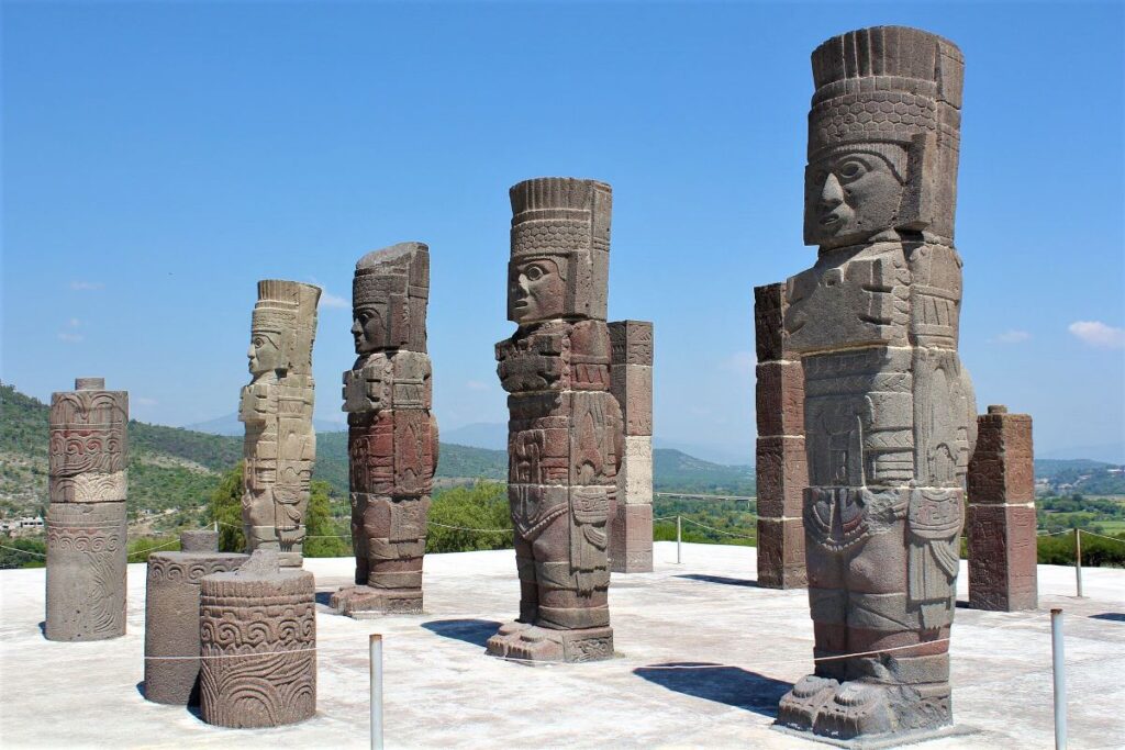 Stand-up, stone carvings of Tula Warriors on display outdoors with a protective railing preventing people from touching them, all outside Mexico City.