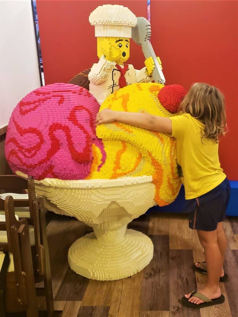 Little Man hugging a very large lego ice cream build with two scops of ice cream in a bowl with a lego chef figurine on top holding a spoon.