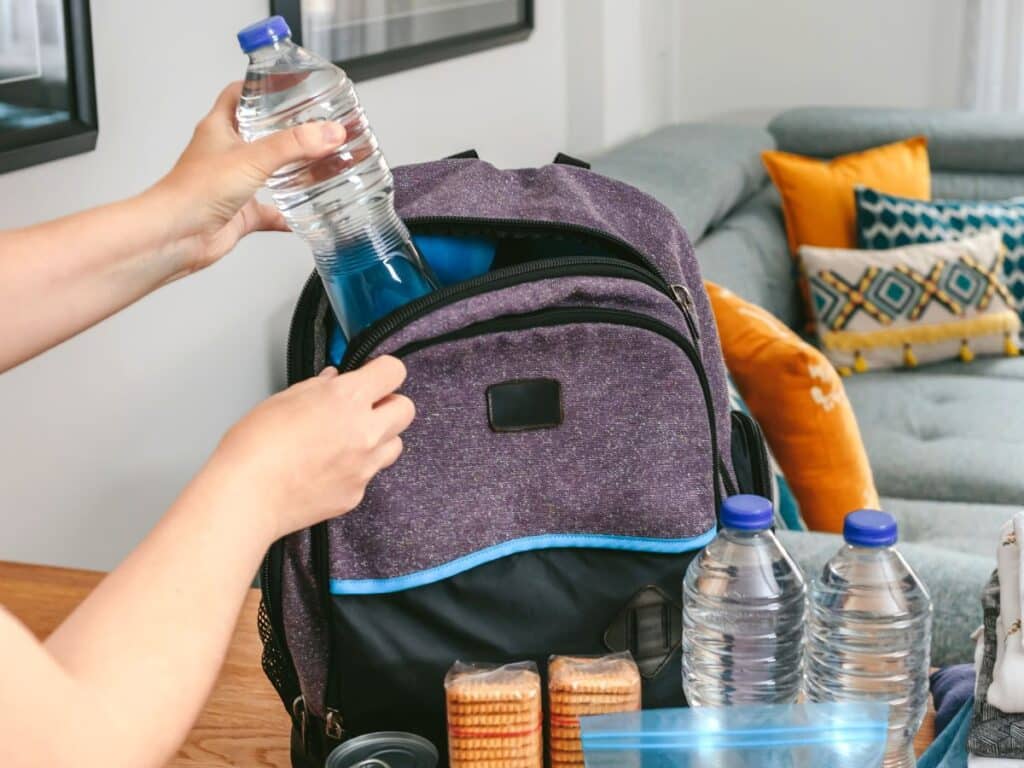 Woman's hands packing a water bottle into a day bag that is sitting on a table next to a couch.