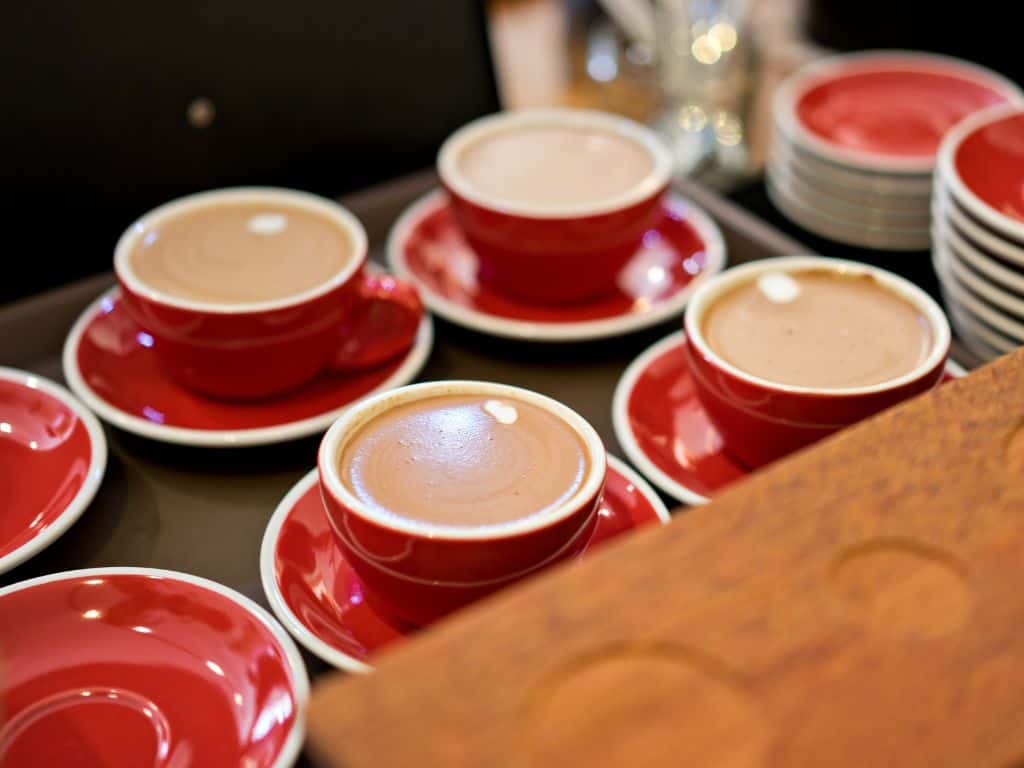 A tray of red coffee cups on saucers that are filled with coffee.