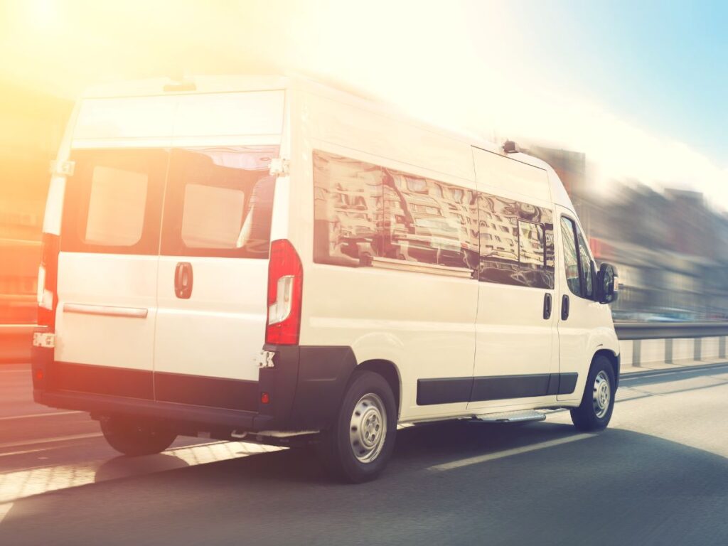Shuttle van driving down a highway as the setting sun casts a shadow from the top left corner.