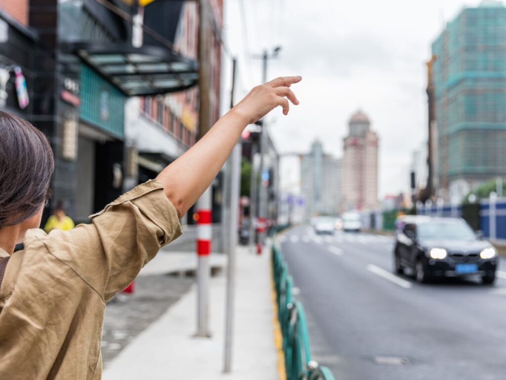 Woman in a tan shirt hailing a taxi on the street.