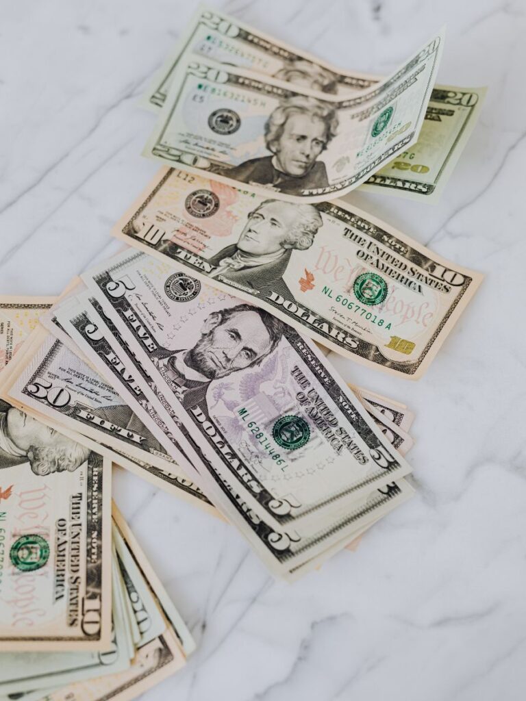Various denominations of US currency bills laying flat on a marble countertop.