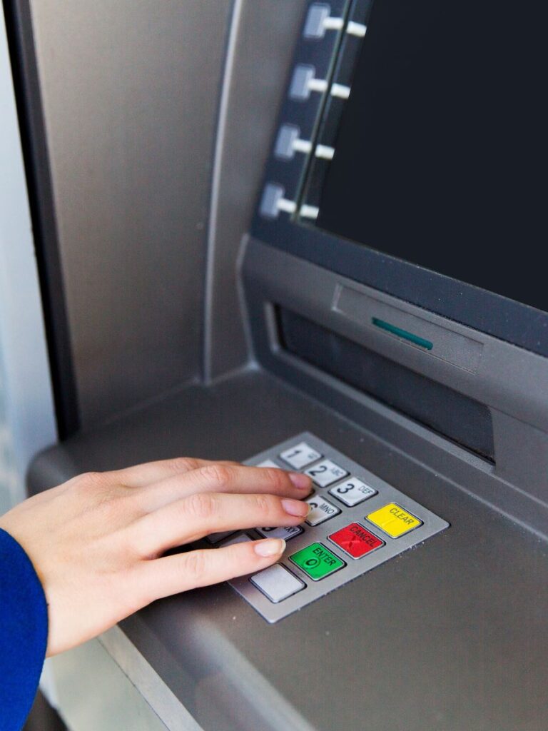 Woman typing her PIN into an ATM.