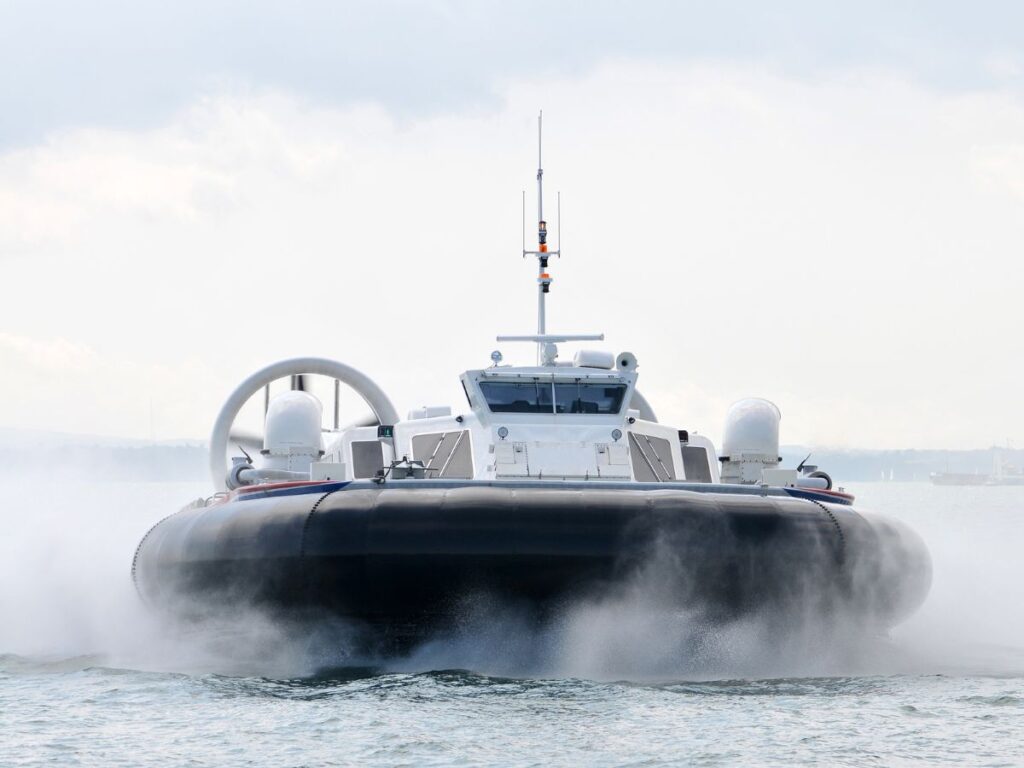 Hovercraft moving through calm water at a fast speed, as shown by the water/mist being sprayed up along the sides.