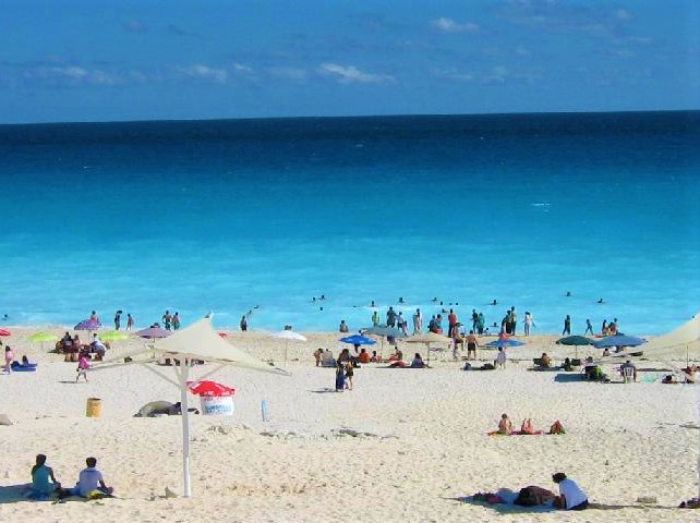 People on a beach in Cancun, with some beach umbrellas scattered throughout.