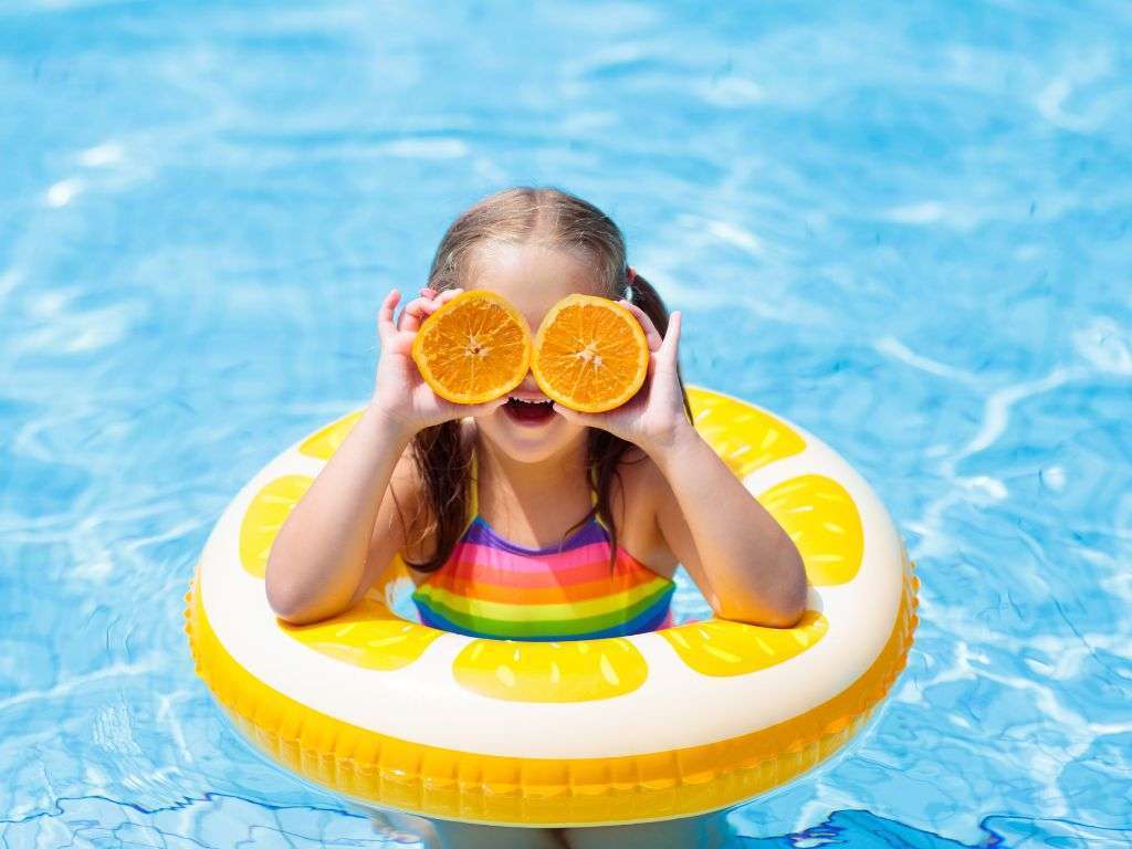 Girl in a lemon shaped floatie in a pool holding orange slices over her eyes
