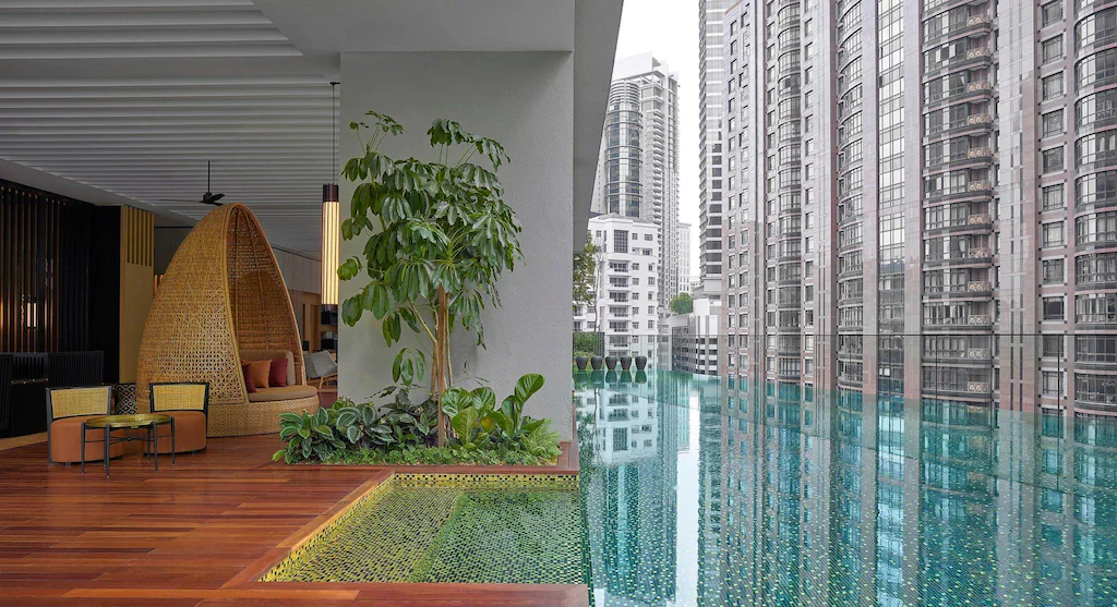 Lengthwise view of the RuMa hotel rooftop pool in Kuala Lumpur. Some of the wood paneled pool deck with lounge chairs is also shown.