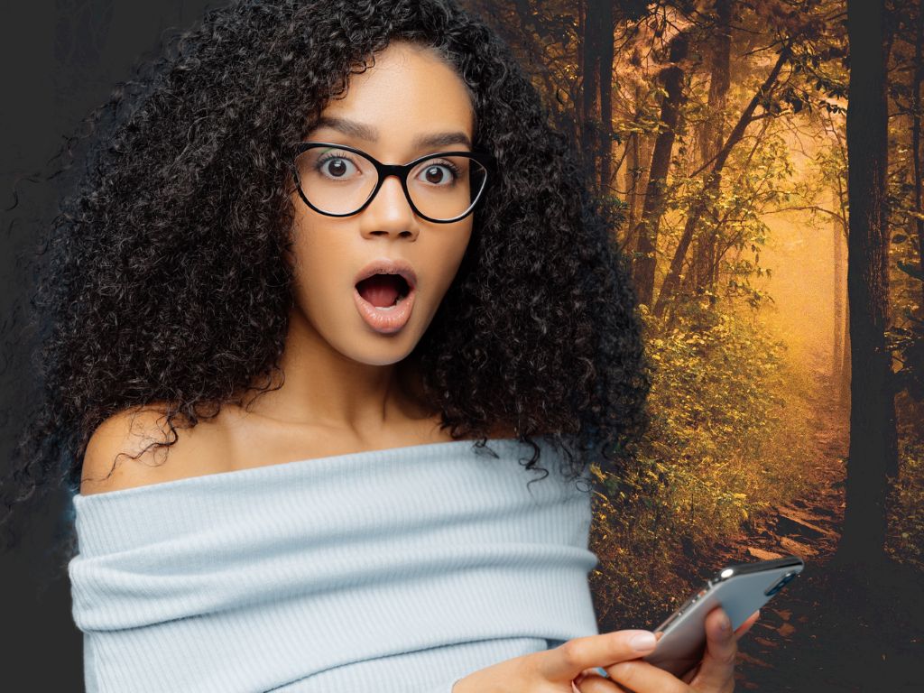 woman holding a smartphone in front of spooky trees