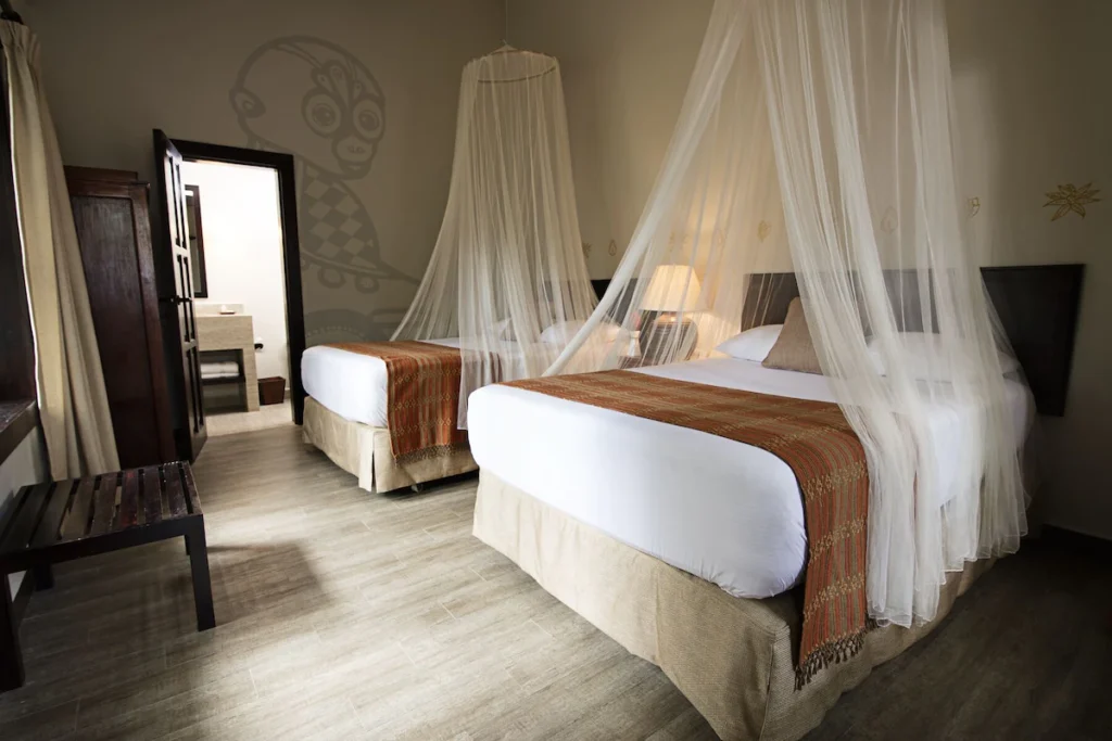 Guest room at Jungle Lodge Hotel with two double beds. There are mosquito nets over the beds and a door to the adjoining bathroom on the far side.
