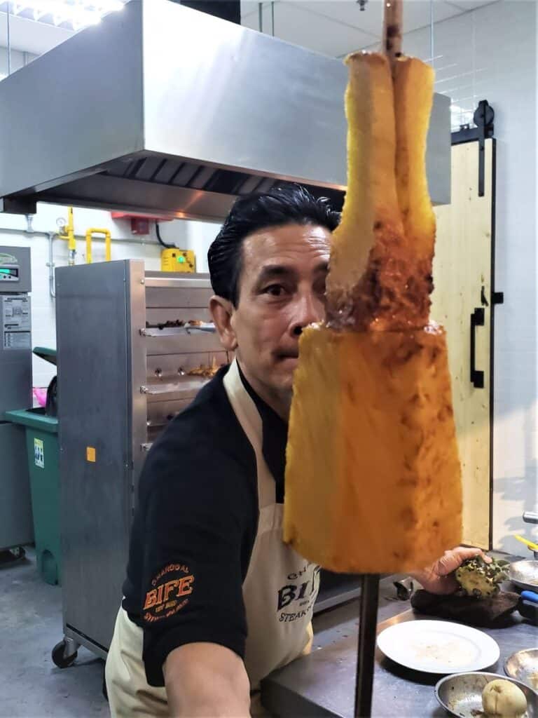 Chef at Bife Charcoal Steakhouse showing off a skewer of roast pineapple close up.