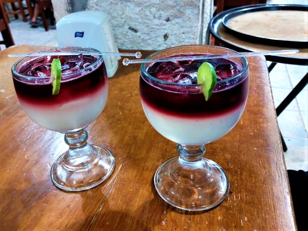 Two sangria/margarita mixed drinks sitting next to each other on a wooden table. Each one has a lime slice resting on the glass rim.