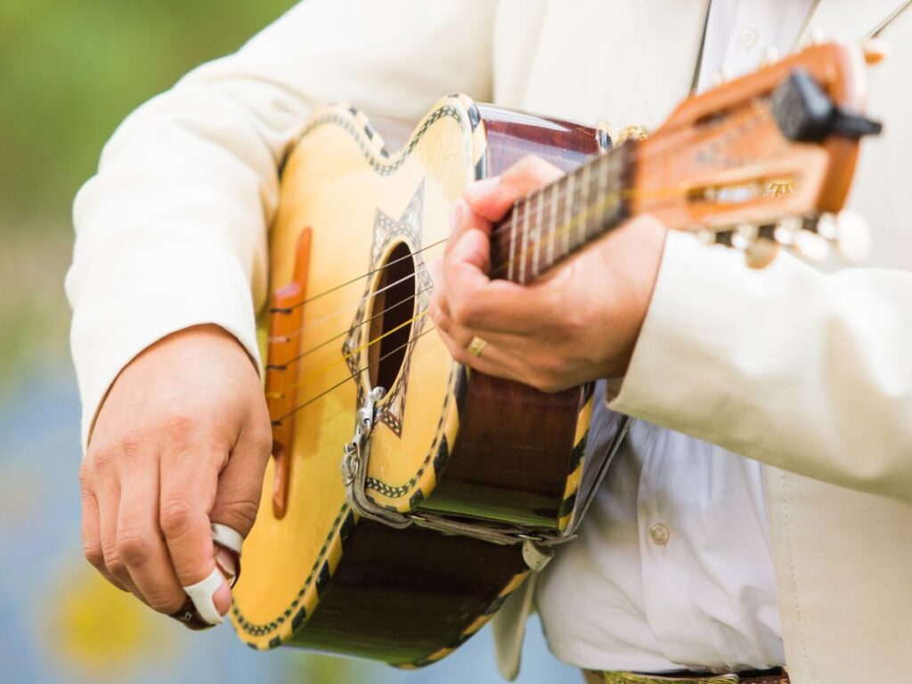 Close up of a guitar being held by a man in a white button down shirt with a white suit jacket on top.