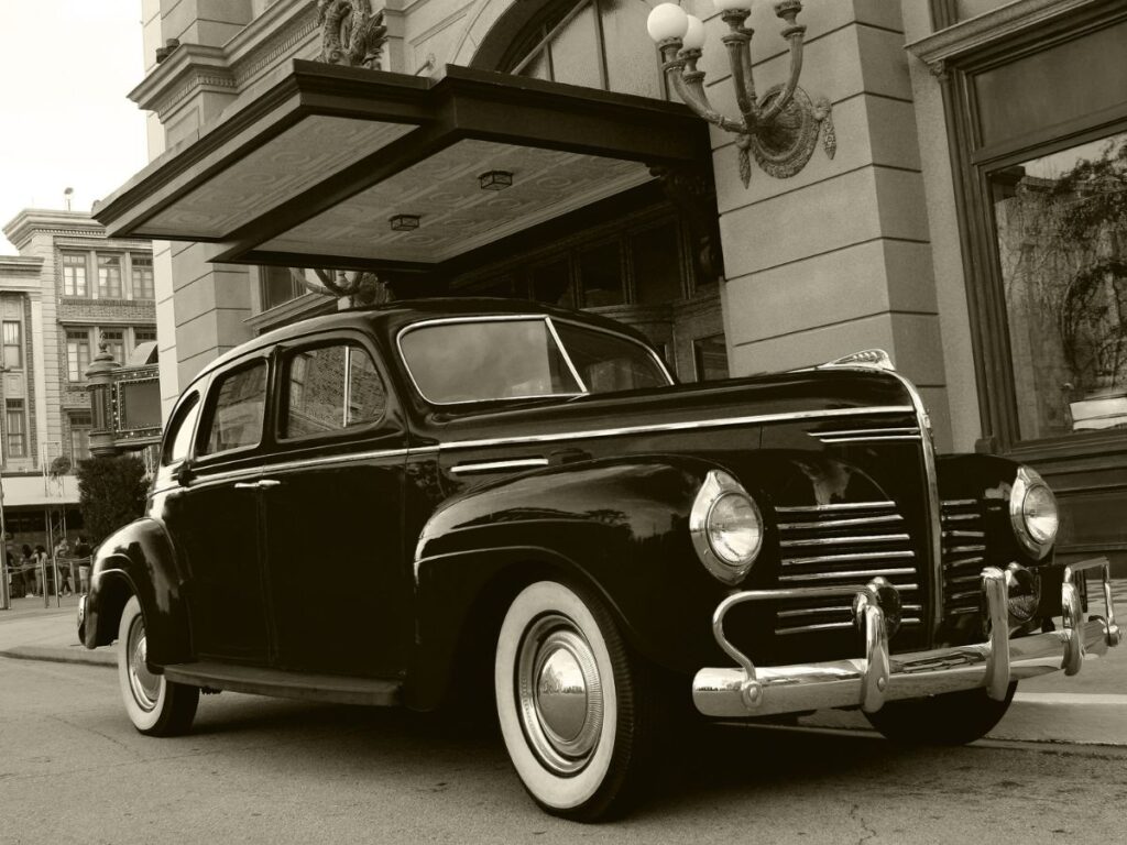 Old fashioned car parked in front of a building in sepia-toned photo style.