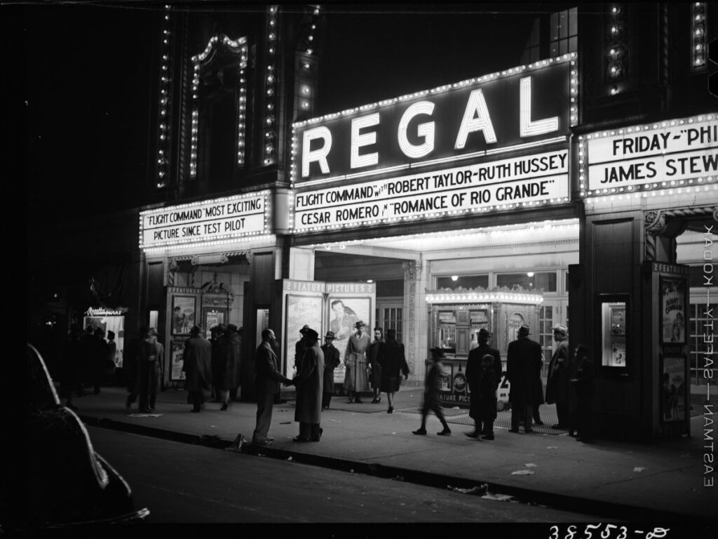 Black and white photo at night of the Regal theatre in Chicago. People are talking past and standing in front of the theater.