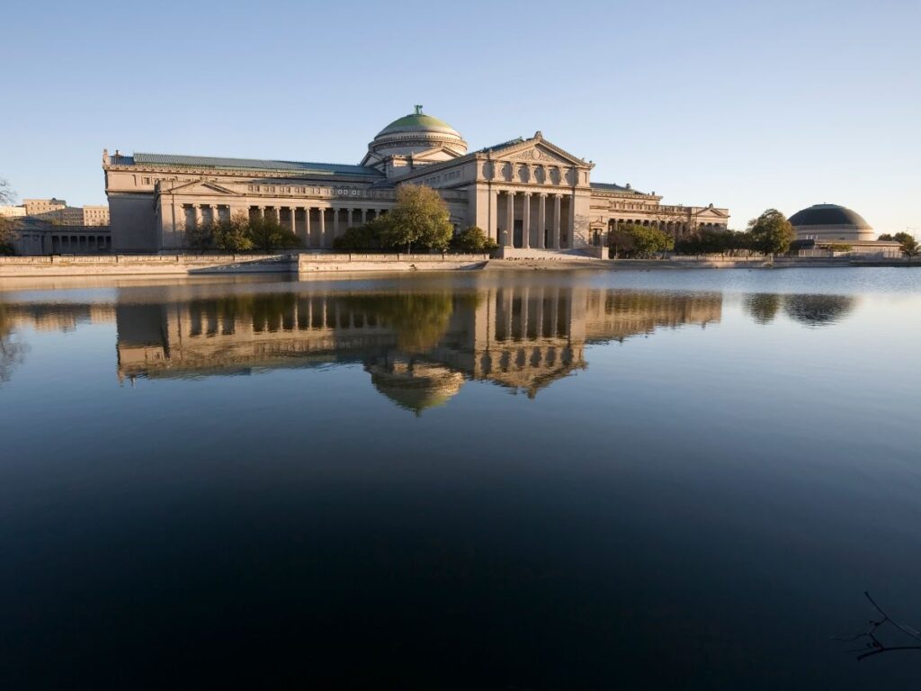 Waterfront view of the Center of Science and Industry in Jackson Park Chicago. The museum is reflected in the still water.