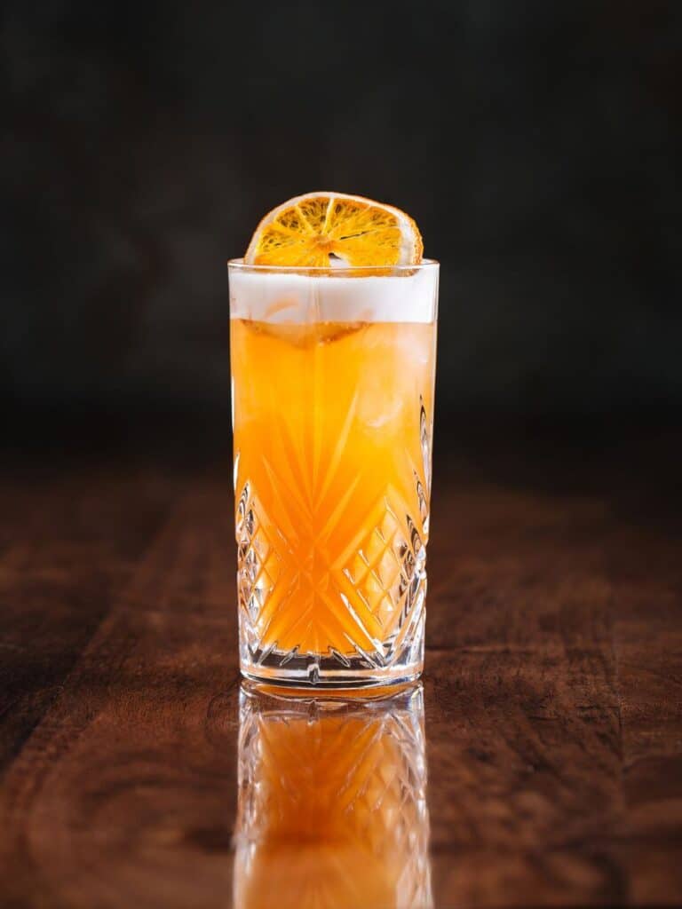Orange mocktail (alcohol free cocktail) on a dark wood table with a darkened background. There is a slice of orange resting on top of the drink.