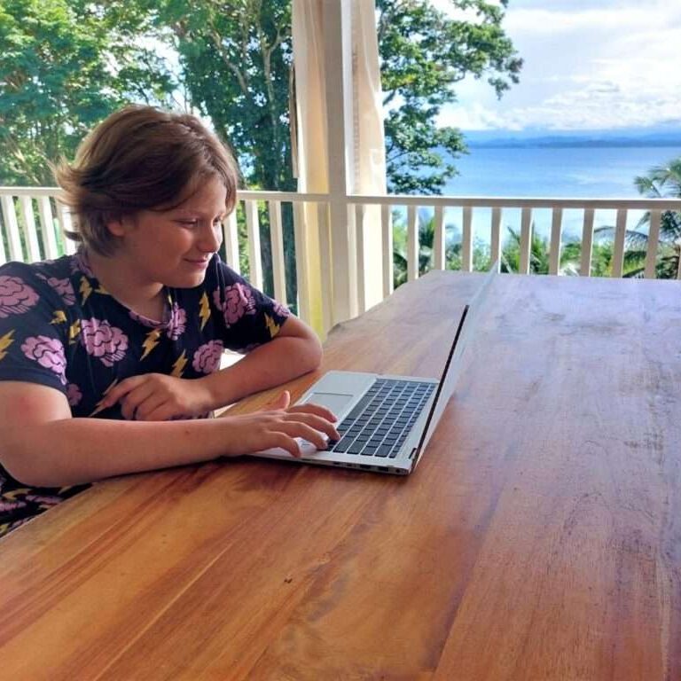 Little Man sitting at a wood table outdoors on a laptop in Bocas del Toro Panama