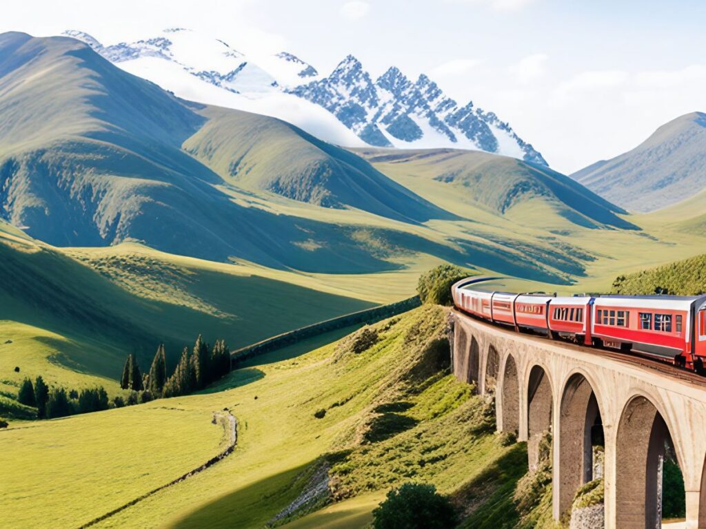 Train on a cobblestone bridge with green valleys and snowcapped mountains in the background.