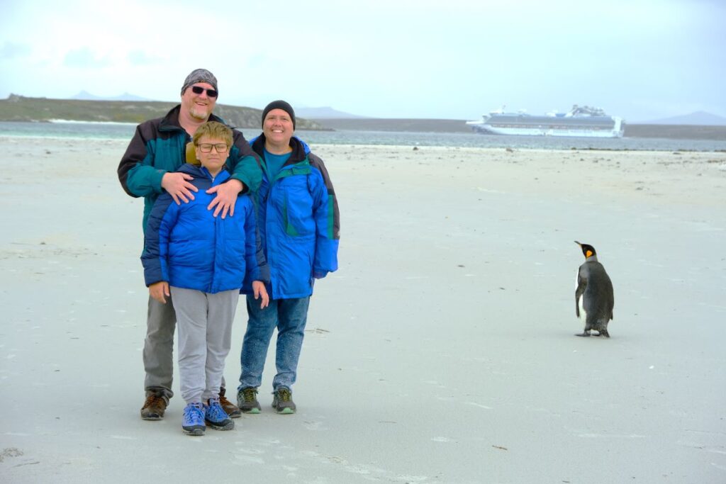 Ouf family with a king penguin on the beach with a cruise ship in the background