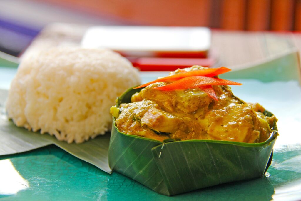 Close up view of fish amok in a banana leaf and white rice, sitting on a table.