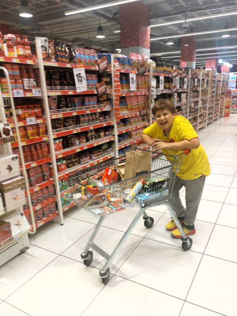 LIttle Man at the grocery store with a shopping cart of food