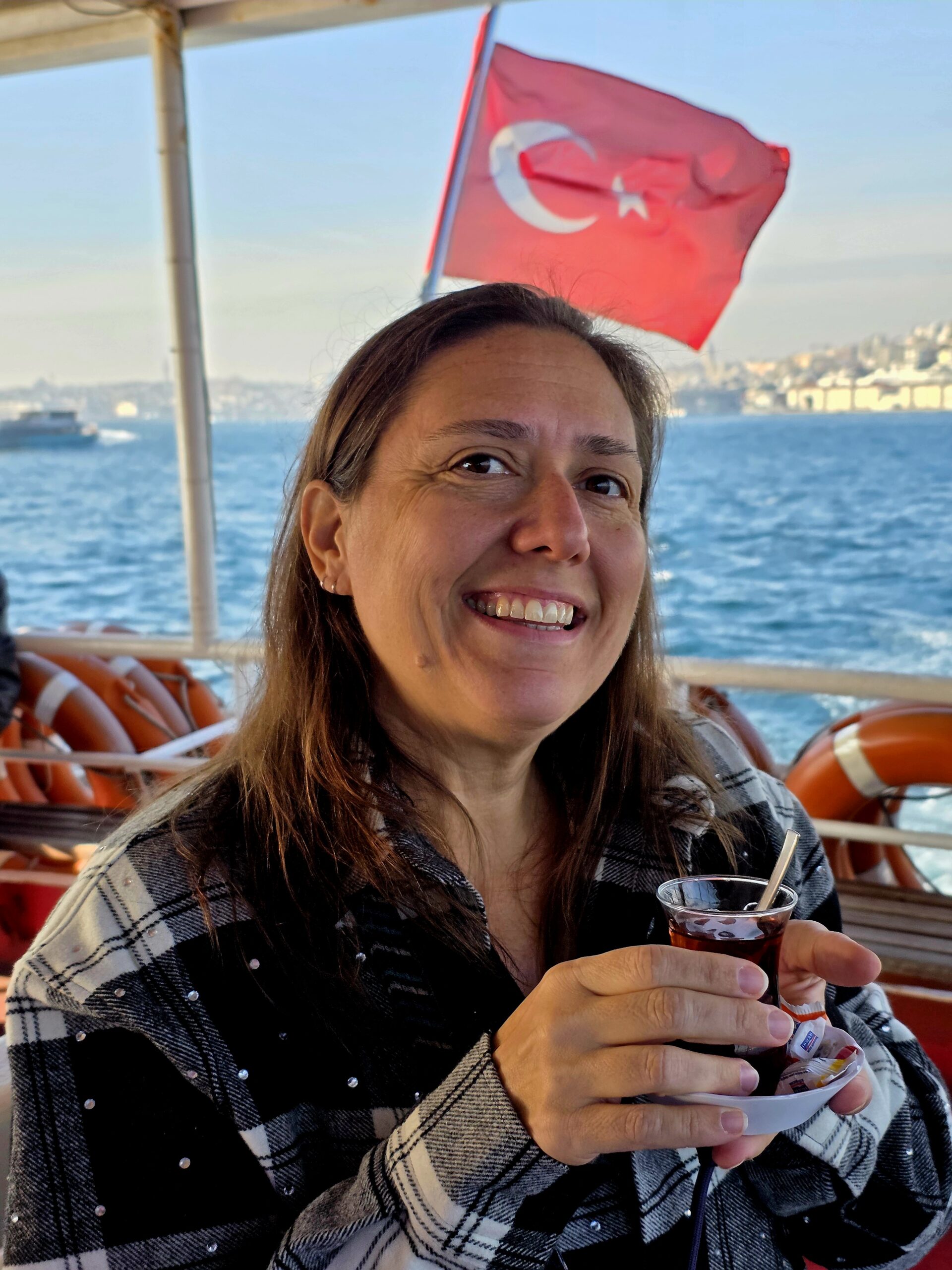 Brodi on a ferry in Istanbul drinking tea with the Turkish flag behind her.